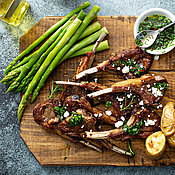 Gebratenes Lammkotelett mit grünem Spargel und Kartoffeln auf Holzbrett